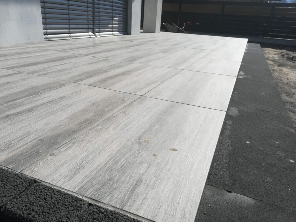 Układanie kostki brukowej na tarasie z płyt imitujących drewno, z widocznym obrzeżem z kostki brukowej. - Władysławowo